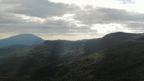 The sun breaks through the clouds in the mountains, illuminating the valley Stock Footage 223481396