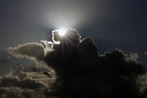 The sun breaks through dark storm clouds, casting a radiant glow on the silve Stock Photos