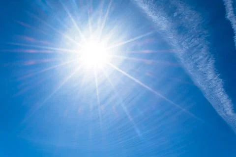 The sun with bright rays in the blue sky with white light contrail clouds fro Fotos Stock