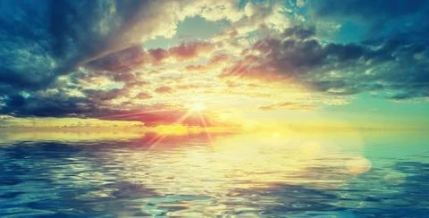 Sun bursting through colourful clouds reflected on calm water Stock Photos