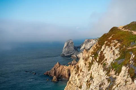 The sun casts a warm glow on rugged cliffs above tranquil waters with a mis.. Stock Photos