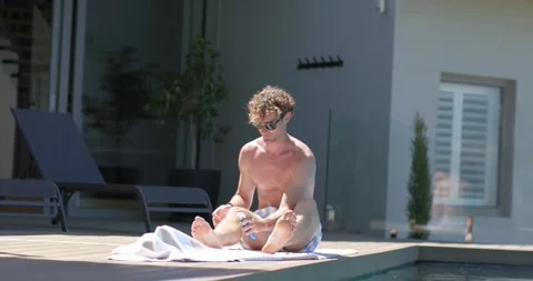 Sun causing man shirtless wearing shades on white towel at pool squeezing bottle Stock Footage 338168376