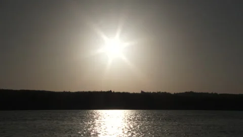 Sun Centered Over Silhouetted Trees And Water Stock Footage 164996479