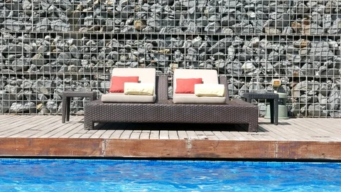 Sun chairs next to a pool at a resort with a rock wall and a deck Video stock 104631266