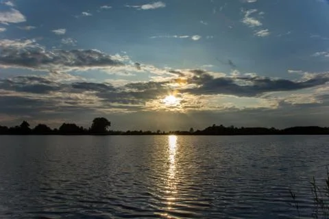 Sun in the clouds and reflecting light in the water of the lake Stock Photos
