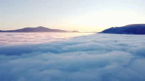 Sun coming up from behind the snow-covered mountains illuminates the sea of clou Stock Footage 227188348