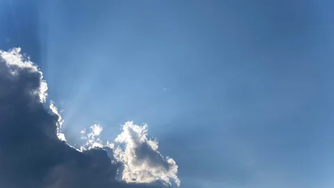 Sun creating sunbeams behind white cloud on blue sky. Stock Footage 128344284