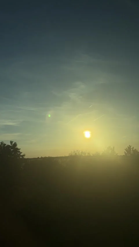 Sun descending behind a verdant tree line, golden light fading into twilight, Stock Footage 336720447