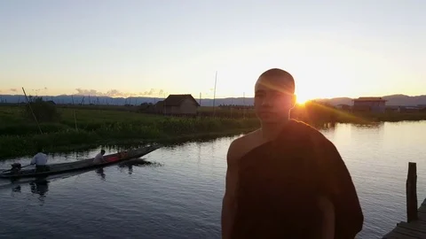 Sun descends on hills behind monk, closeup, boat sails, stilt houses, Inle Lake Видео 79973764