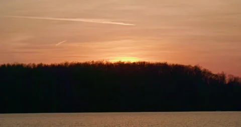 The sun dipping behind a tree line at the lake Stock Footage 263933664
