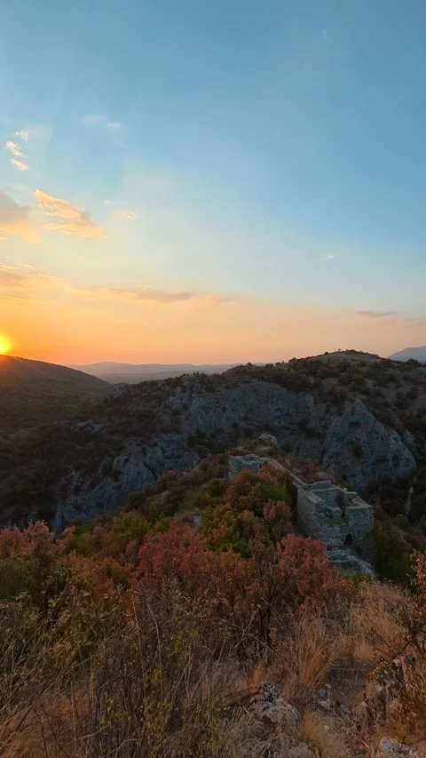 Sun dips behind rugged cliffs, painting sky in warm hues. Soko Grad, Vertical 動画素材 345898031