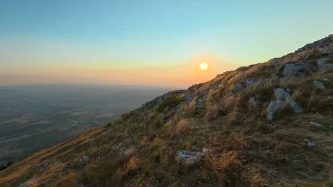 Sun dips behind rugged hilltop, casting golden glow. Mount Rtanj sunrise Serbia Stock Footage 344686419