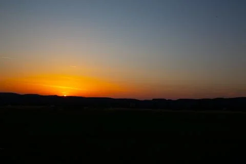 The sun dips below the horizon, creating a stunning sunset over the hills w.. Stock Photos