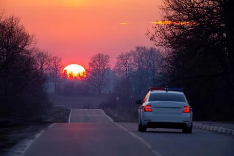 The sun dips below the horizon over the road and police car Stock Photos