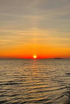 Sun dips below horizon over calm waters, casting warm orange glow across sky  Stock Photos