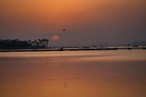 Sun dips low, casting warm glow over calm water Stock Photos
