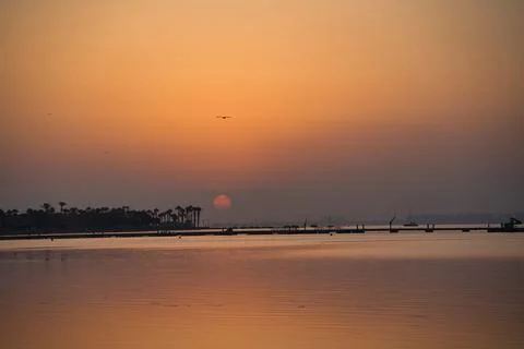 Sun dips low over calm water, casting warm hues Stock Photos