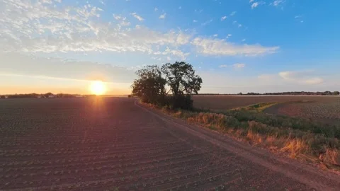 Sun dips low over tilled earth and winding dirt path. Golden light spills Stock Footage 343696637