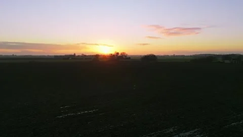 Sun dips low, painting sky in soft amber hues. Silhouetted fields stretch wide Stock Footage 343695883