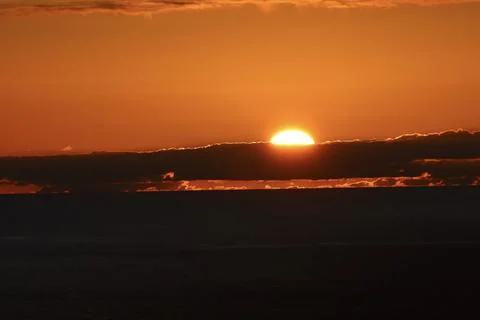 Sun disappearing behind clouds above the Atlantic Ocean at sunset Stock Photos