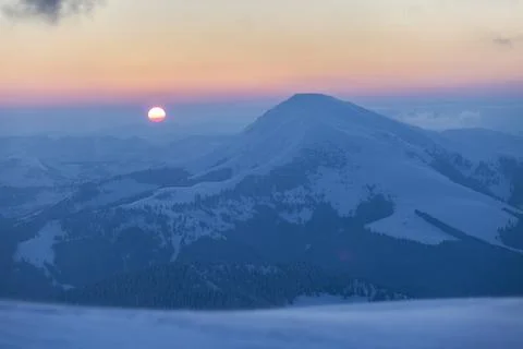 The sun disk rises above a snow-covered mountain at dawn 스톡 사진