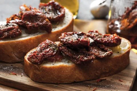 Sun-dried tomatoes on the white bread on the wooden board Stock Photos