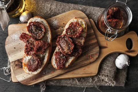 Sun-dried tomatoes on the white bread on the wooden board Stock Photos