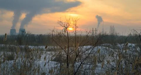 The sun in the evening sky framed by tree branches and factory smoke Foto stock