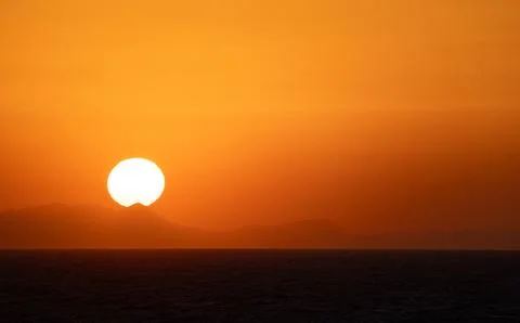 The Sun Falling Behind Mountain peak with sea foreground. A Spectacular golden Stock Photos