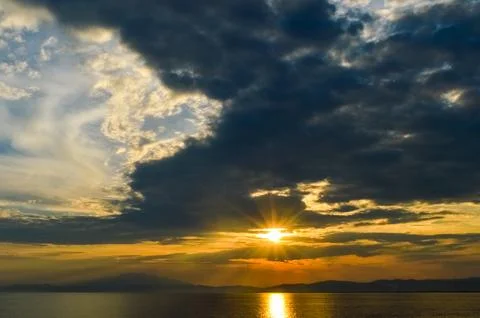 Sun flare and dramatic clouds over sea at sunset from ferry to Thasos. Stock Photos
