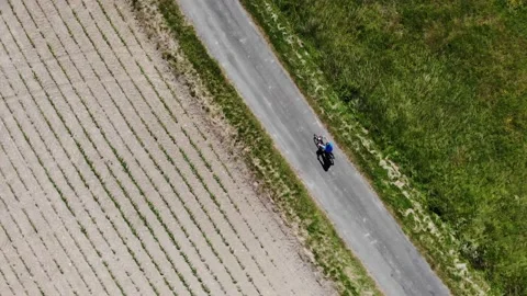 SUN FLARE, DRONE: Flying behind unrecognizable man riding his bicycle at sunrise Video stock 132049861