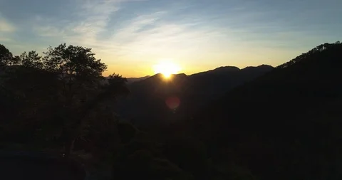 Sun flickers through tree at dawn on mountain road drone aerial 4k Stock Footage 125754247