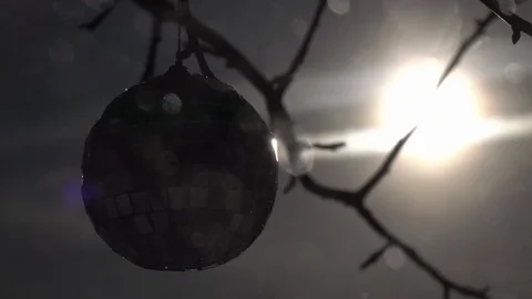 Sun in frame, lens flare and Christmas tree ball, rotating on branch in snowfall Stock Footage 87872671
