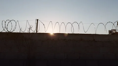 Sun glare behind barbed wire fence on the top at sunset with clear sky creating Stock Footage 336589830
