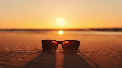 Sun Glasses On Sandy Beach, At Sunset With Wind And Slow Motion Static Shot Stock Footage 325840145