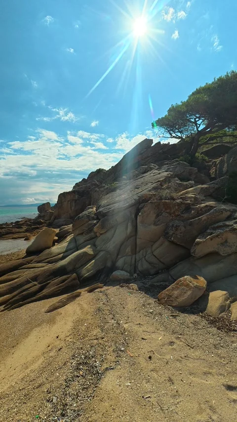 Sun glints off rocks beside calm sea waters. Trani Ammouda, Vertical Stock Footage 340651734