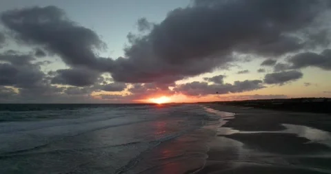 The sun goes down over the sea while you see people kitesurfing. 動画素材 261074501