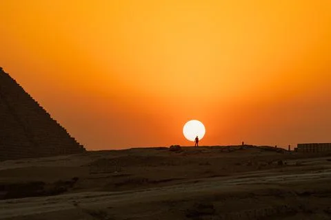 The sun is going down behind the pyramid and a silhouette of a man standing on Stock-Fotos