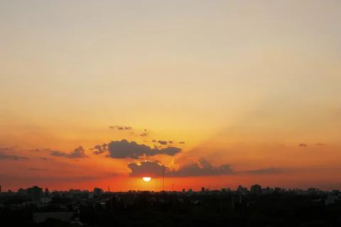 Sun hanging from a cloud above backlit city skyline from aerial view Stock Photos