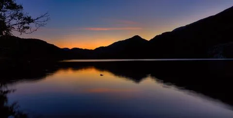 The sun has set behind the mountains around Llyn Gwynant, a lake in Snowdonia Stock Photos