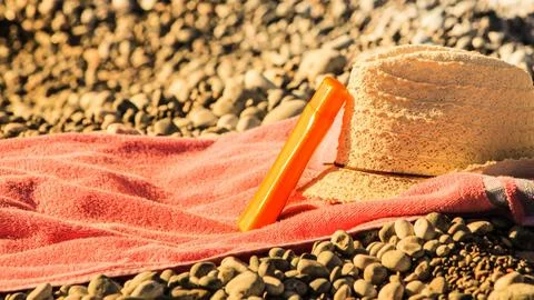 Sun hat and sunscreen on stone beach Stock Photos