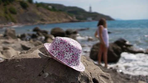 Sun hat lying on stone on pebble beach of blue sea 스톡 사진