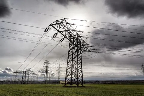 Sun hidden behind dramatic clouds and electricity pylons conducting current Stock Photos