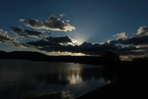 Sun hide behind the clouds, reflection on lake. Stock Photos