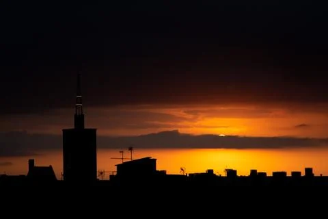 Sun is hiding behind the clouds at sunset, roof top view of an old church tower. Stock Photos