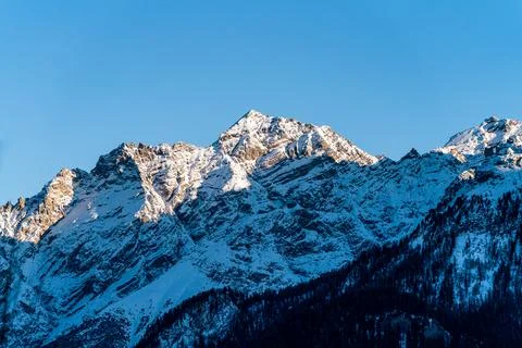 Sun hitting sharp mountain peaks covered in snow Stock Photos