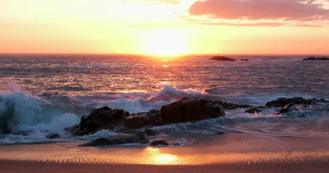 Sun on horizon at sunset as ocean waves splash against rocks on shoreline. Stock Footage 130422127
