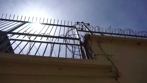 The sun illuminates a very high prison fence with barbed wire, iron bars, high Video stock 110272548