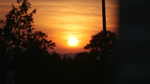 The sun as it sets between two trees in the distance. The sky is golden. Stock Footage 112020949