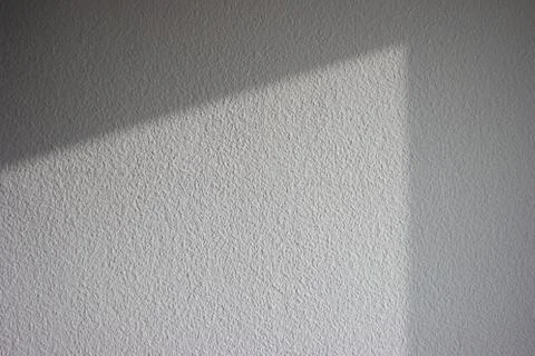 Sun light casting angular shadow on gray interior textured wall Stockfoto's
